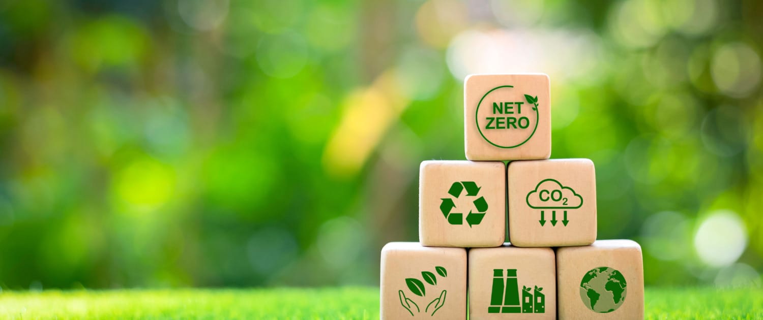 Wooden blocks representing sustainability with symbols of net zero emissions, CO2 reduction, recycling, and global environmental responsibility, highlighting the shift toward eco-friendly practices in global supply chains and contract manufacturing.