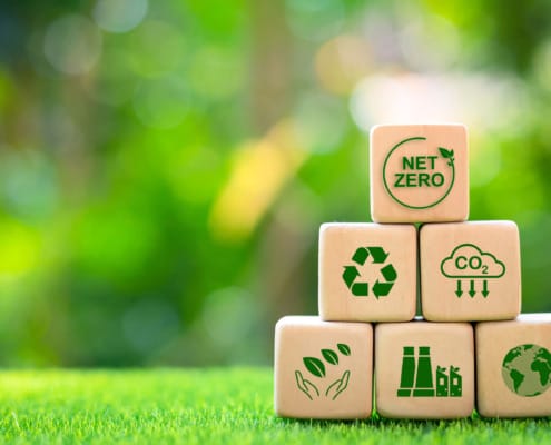 Wooden blocks representing sustainability with symbols of net zero emissions, CO2 reduction, recycling, and global environmental responsibility, highlighting the shift toward eco-friendly practices in global supply chains and contract manufacturing.