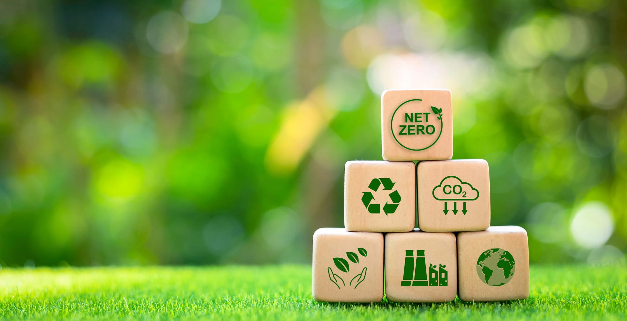 Wooden blocks representing sustainability with symbols of net zero emissions, CO2 reduction, recycling, and global environmental responsibility, highlighting the shift toward eco-friendly practices in global supply chains and contract manufacturing.