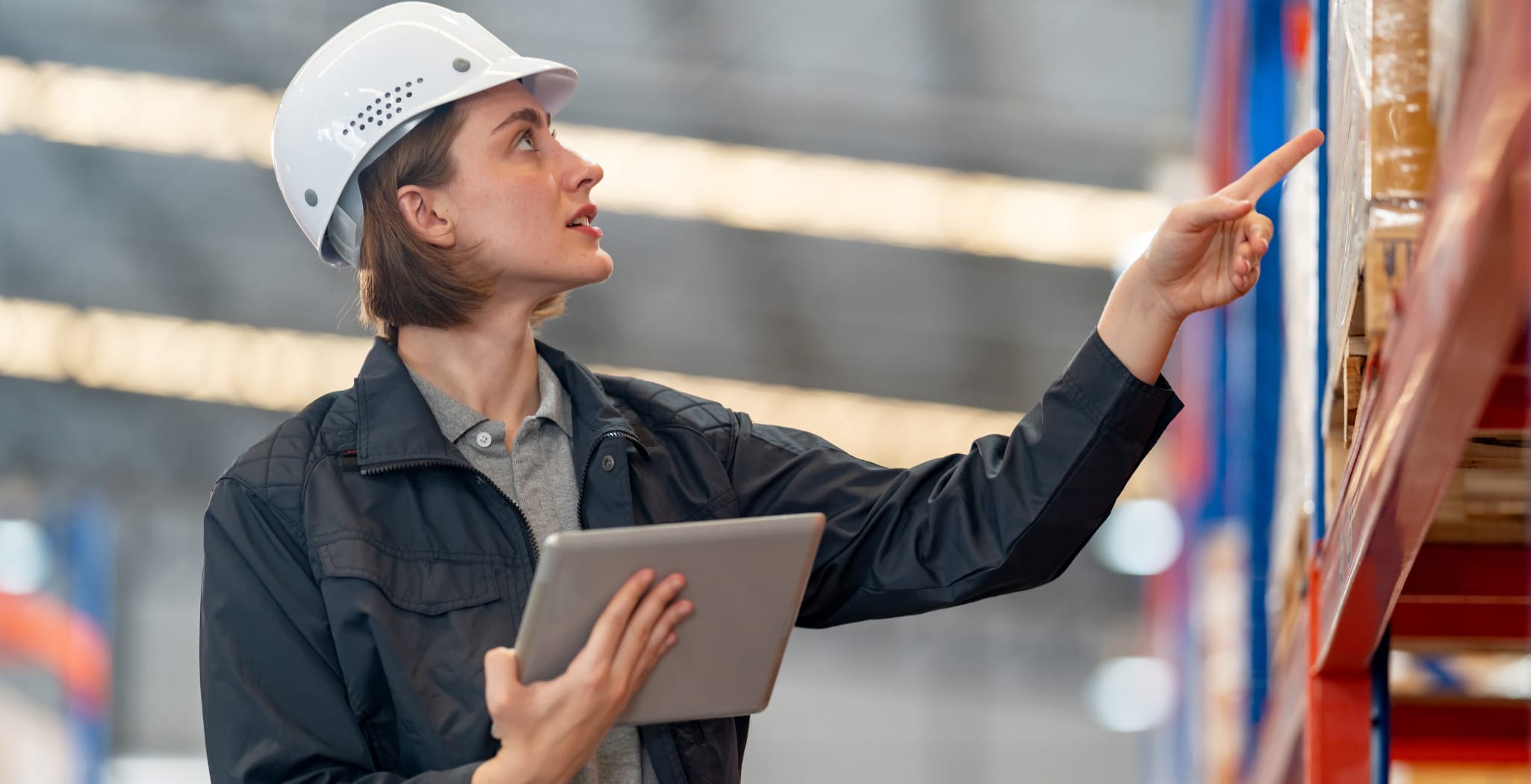Female supply chain inspector in a warehouse performing photo verification of packaged goods, using a tablet to document product quality and location.